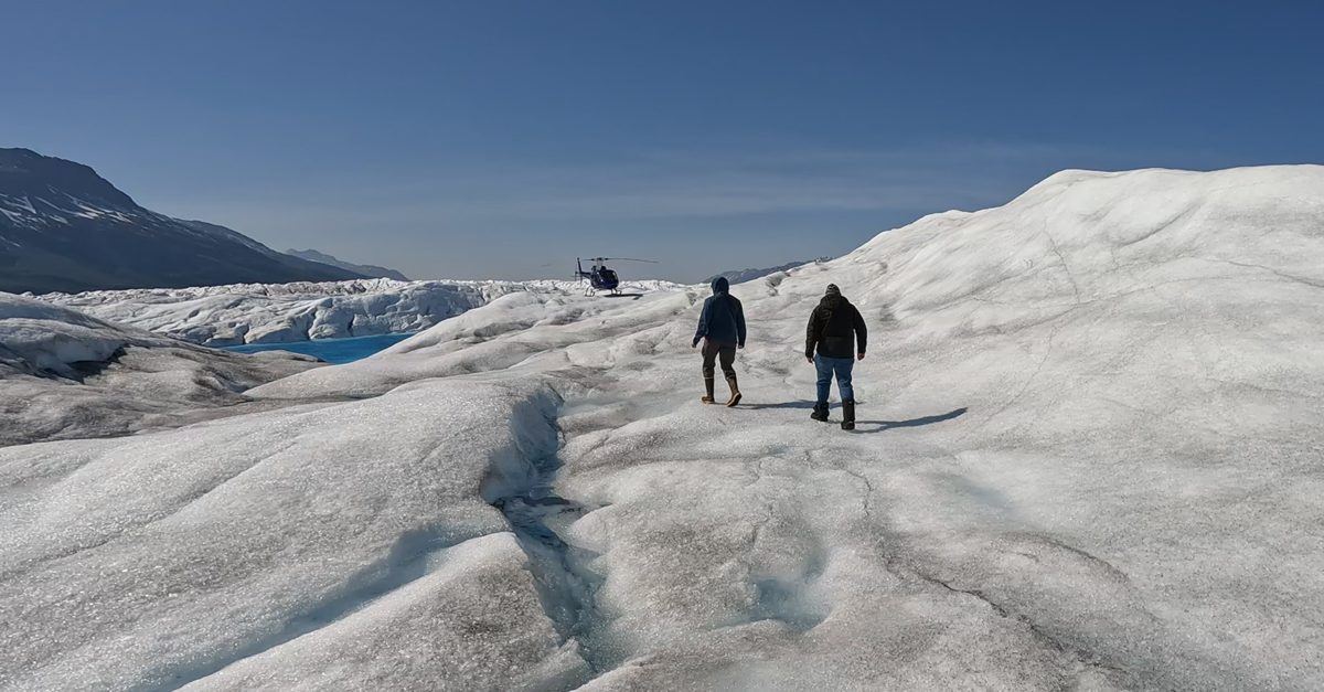 Two people walking across an Alaska glacier toward a helicopter