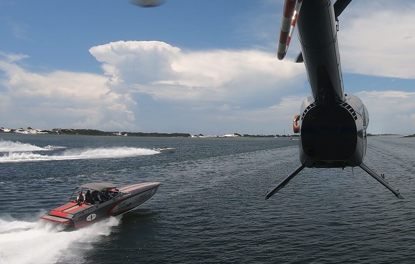 View from a camera helicopter skid over a red offshore powerboat at speed